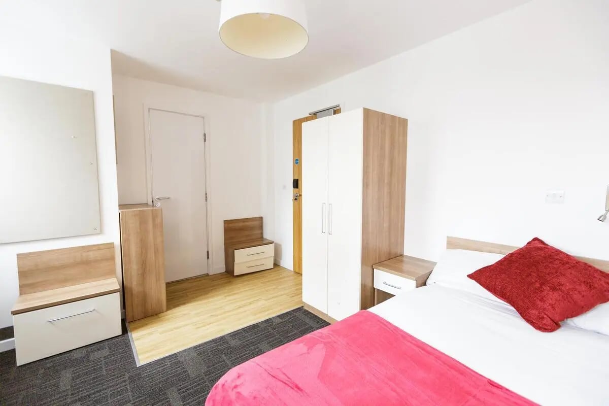 Wardrobe bed with red cushion and pink throw Bedroom at AXO Islington in London Student Accommodation