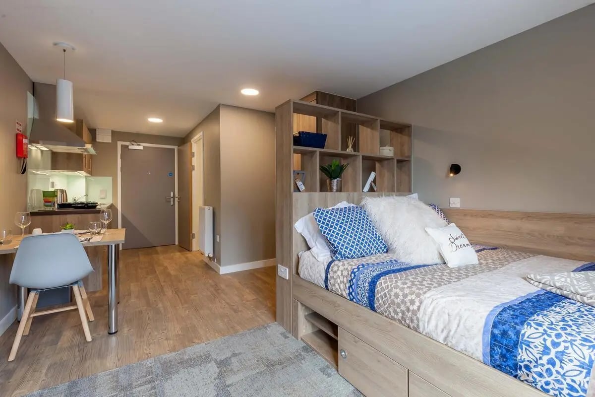 Bed with blue patterned pillows kitchen and desk studio apartment at The Combworks in Aberdeen Student Accommodation