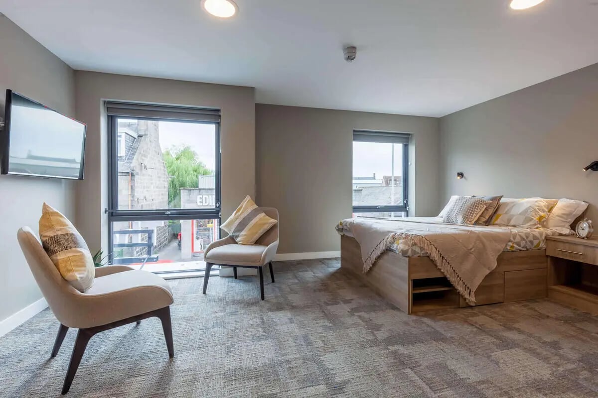 Two chairs bed bedside table tv bedroom at The Combworks in Aberdeen Student Accommodation