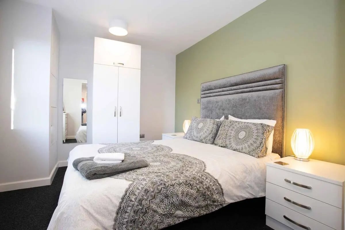 Bed with grey headboard white linens patterned throw bedside table Bedroom at Singer Hall in Coventry Student Accommodation