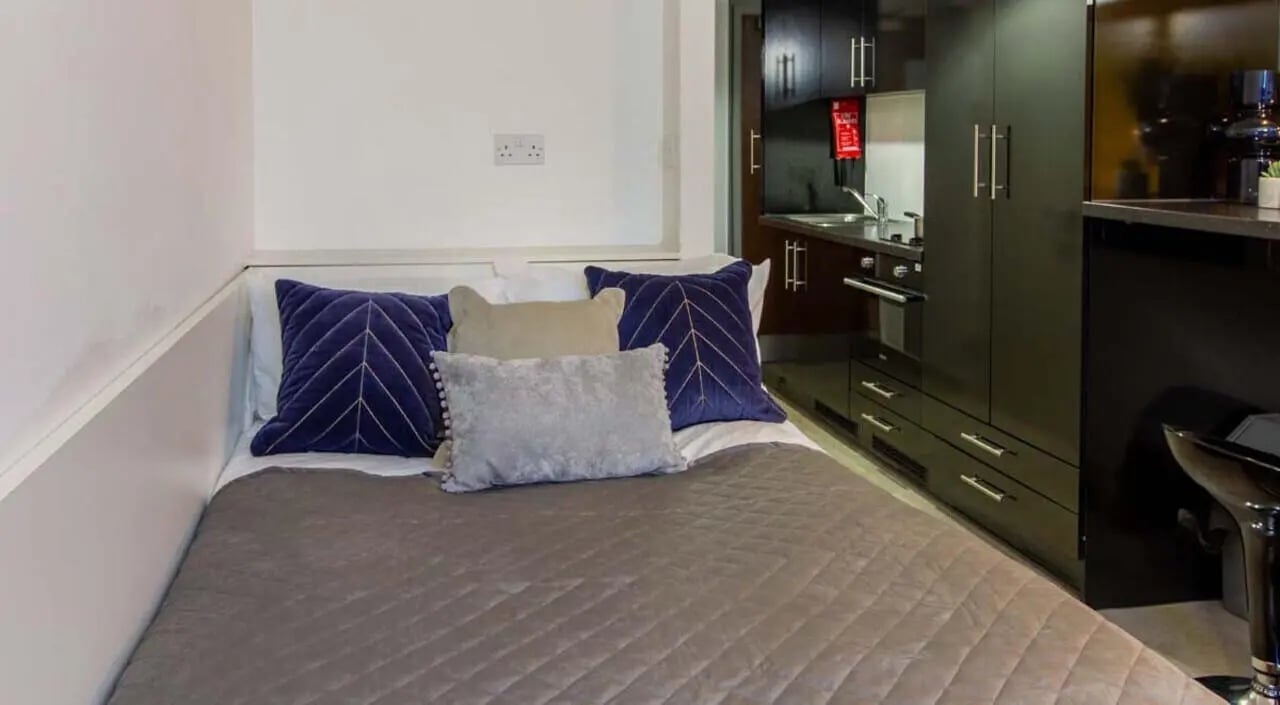 Bed with blue pillows, kitchen, and closet studio apartment at Bowman House in Nottingham Student Accommodation