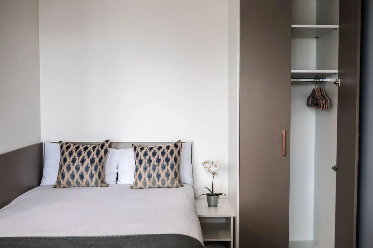 Bed with patterned pillows and open wardrobe bedroom at McDonald Road in Edinburgh Student Accommodation