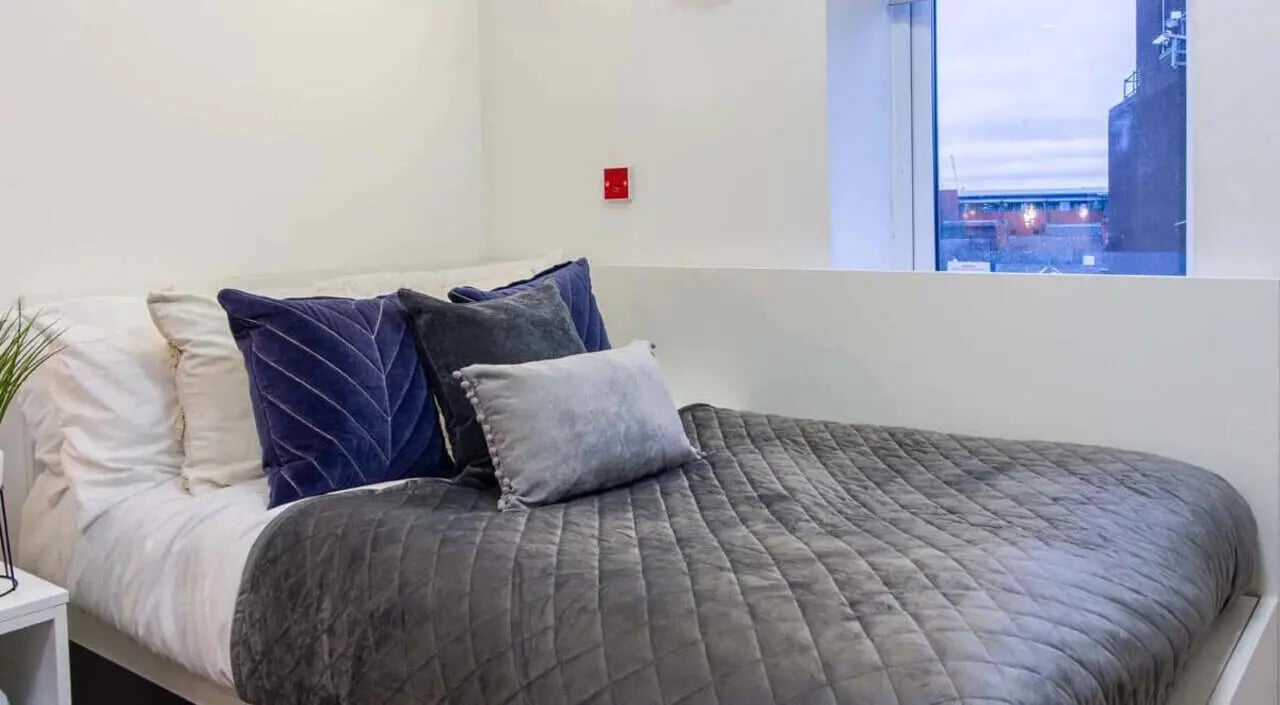 Bed with grey quilted blanket blue pillows bedroom at Bowman House in Nottingham Student Accommodation