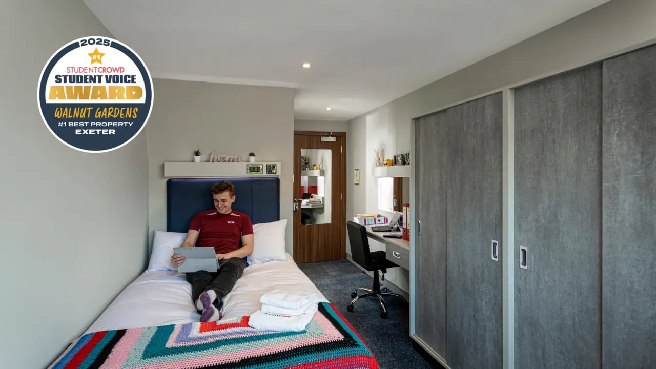 Man using laptop on bed desk and wardrobes bedroom at Study Inn Walnut Gardens Exeter in Exeter Student Accommodation
