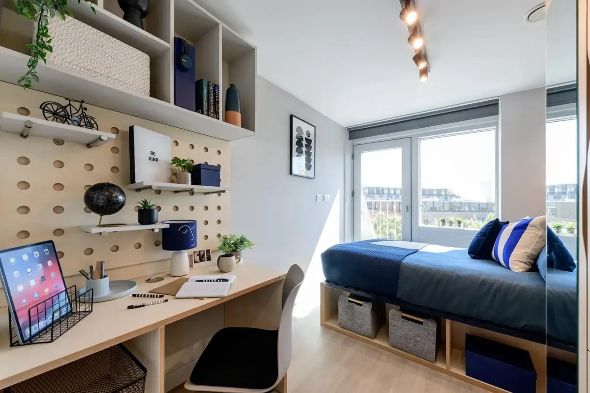 Desk tablet shelving lamp bed with pillows bedroom at Wick Park in London Student Accommodation