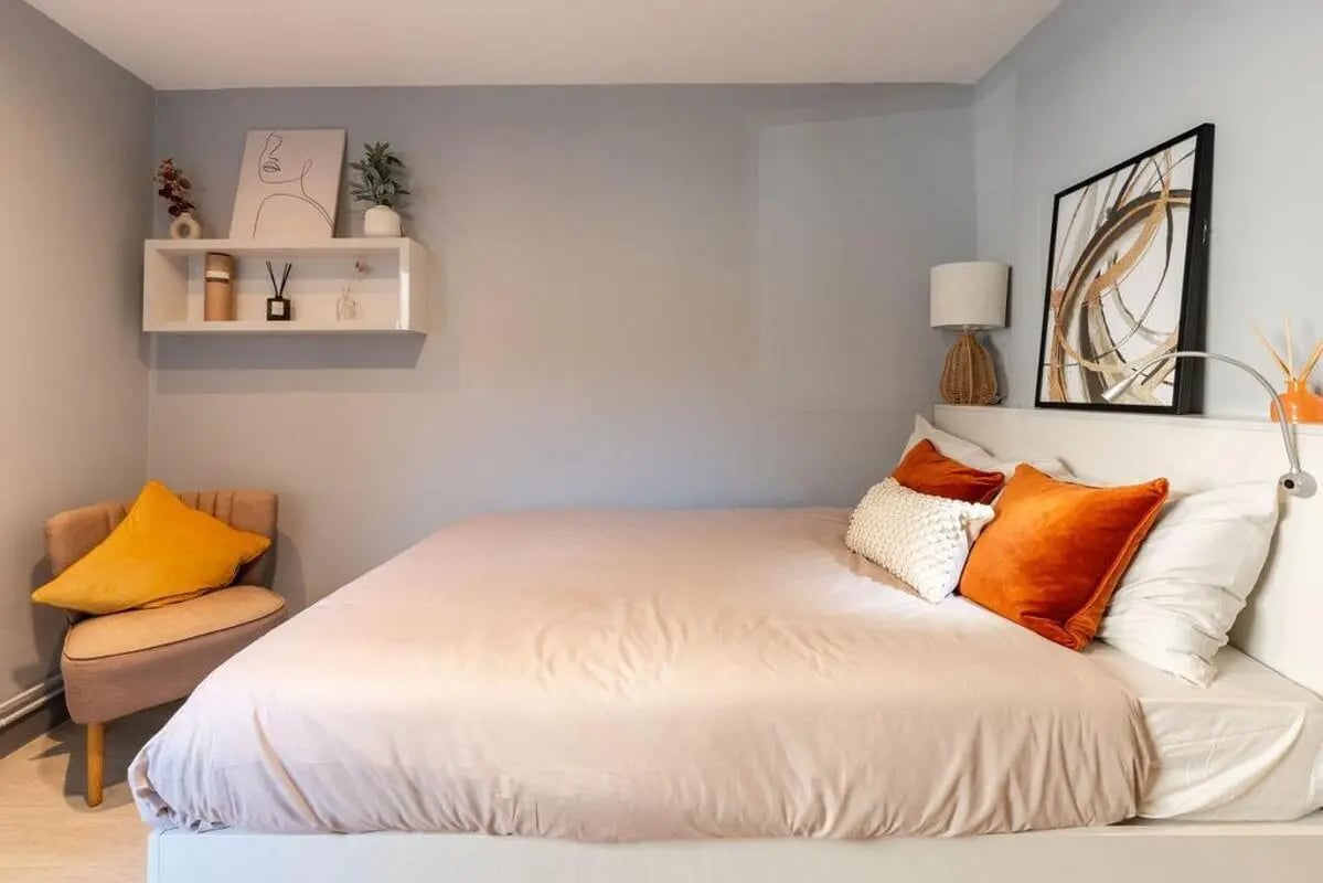 Bed with orange pillows white bedding and chair bedroom at The Walls in Southampton Student Accommodation