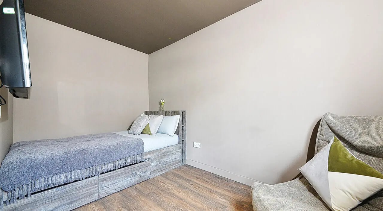 Bed with grey throw and cushions armchair bedroom at Marketgait Apartments in Dundee Student Accommodation