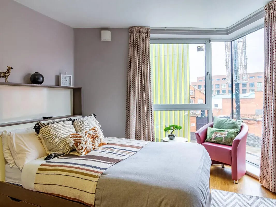 Bed with patterned pillows and pink chair bedroom at Camden Hawley Crescent in London Student Accommodation