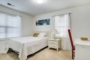 White bed with nightstand and red chair Bedroom at University Woods in Raleigh Student Accommodation