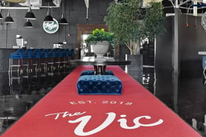 Red carpet with blue tufted ottomans and bar stools common area at The Vic in Greensboro Student Accommodation