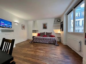 Bed with pillows mounted TV and wooden floor living room at Studio in 73 Rue Saint-Honoré, 75001 Paris, France in Paris Student Accommodation