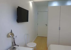 Wall mounted TV desk lamp white chair bedroom closet living room at Ensuite room in renovated apartment in Saldanha - S1 in Lisbon Student Accommodation