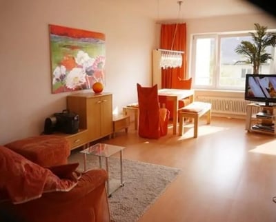 Orange sofa artwork dining table TV living room at Admirable and bright studio in Charlottenburg in Berlin Student Accommodation