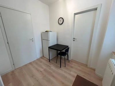 Fridge table chairs and clock kitchen at Minimalist one-bedroom apartment in the center of Bergamo: quiet, bright, and with utilities included in Bergamo Student Accommodation