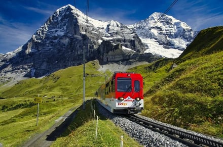 Red train traveling through green mountains exterior