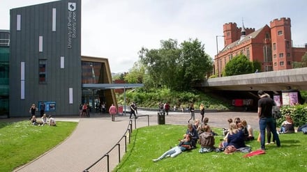 Students relaxing on grass near university building exterior at University Of Sheffield Accommodation