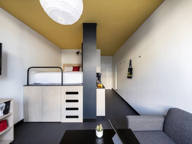 Lofted bed, sofa, and kitchenette modern living area at UKO Newtown in Sydney Student Accommodation