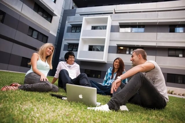 Students sitting grass laptop exterior at UNSW Village in Sydney Student Accommodation