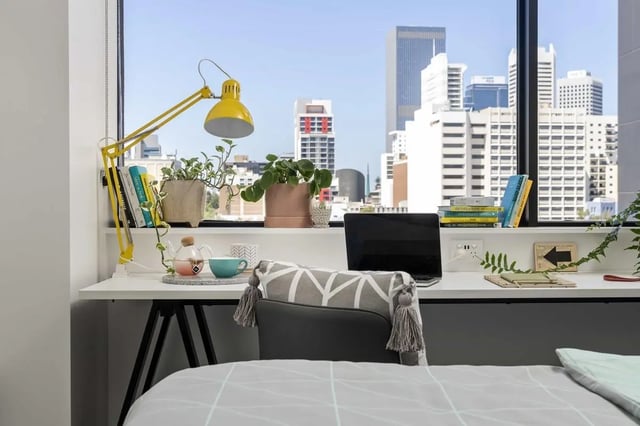 Desk with lamp laptop books plants and city view study area at Campus Perth in Perth Student Accommodation