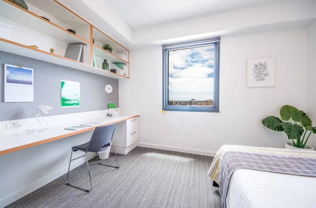 Desk with chair shelves window plant bed bedroom at dwell East End Adelaide in Adelaide Student Accommodation