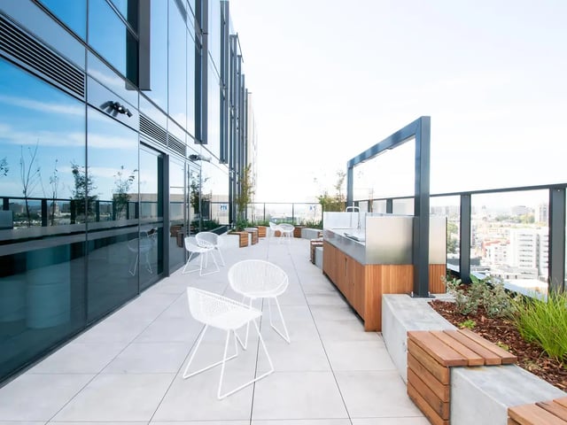 Outdoor kitchen with white chairs and cityscape view exterior at Yugo Berkeley Street in Melbourne Student Accommodation