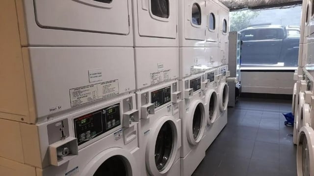 Stacked laundry machines with coin slots and displays laundry room at Student Living on Villiers in Melbourne Student Accommodation