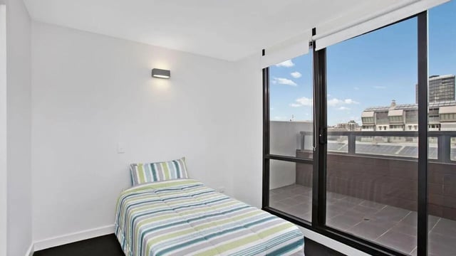 Bed with striped comforter balcony view bedroom at Student Living on Raleigh in Melbourne Student Accommodation