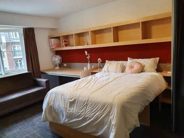 Bed sofa desk shelves and fan bedroom at dwell Village Melbourne City in Melbourne Student Accommodation