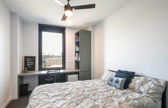 Bed desk bookshelf and ceiling fan bedroom at dwell Village Melbourne City in Melbourne Student Accommodation