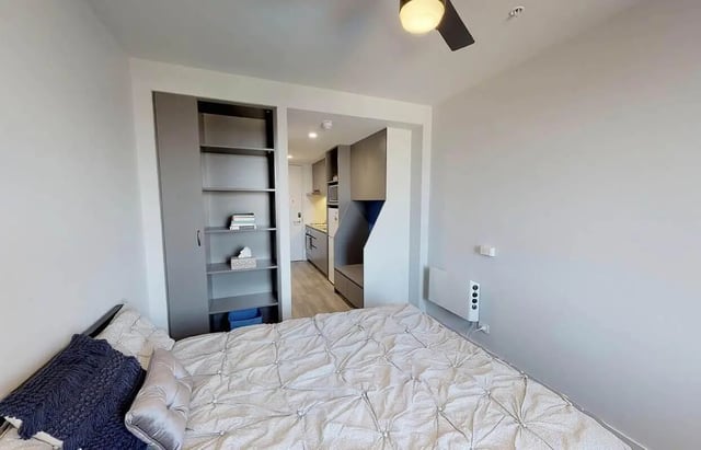 Bed with bookshelf and kitchen area Bedroom at dwell Village Melbourne City in Melbourne Student Accommodation