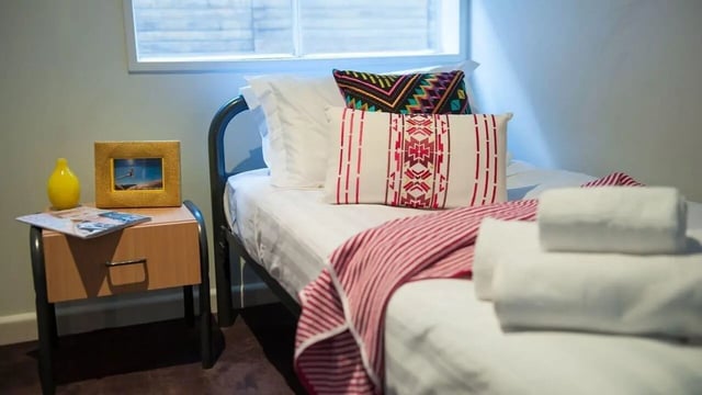 Bed with pillows throws and bedside table Bedroom at Student Living-339 Swanston in Melbourne Student Accommodation