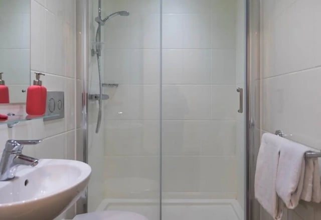 Sink shower with tiled walls and towels bathroom at The Cam Foundry in Cambridge Student Accommodation
