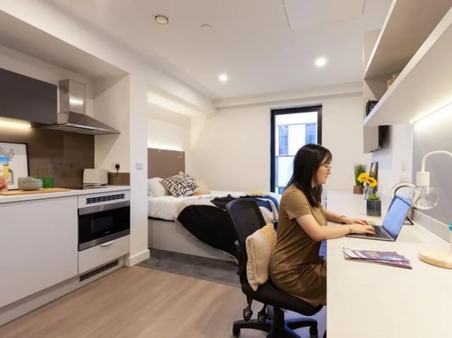 Kitchen bed desk and woman working studio room at True Swansea in Swansea Student Accommodation