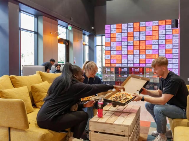 Students sharing pizza on a sofa living room at True Swansea in Swansea Student Accommodation