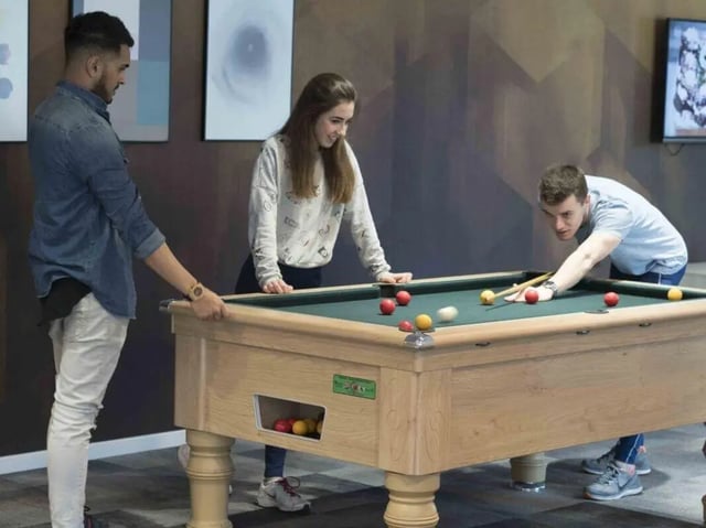 Students playing billiards on a wooden pool table common area at The Railyard Cambridge in Cambridge Student Accommodation
