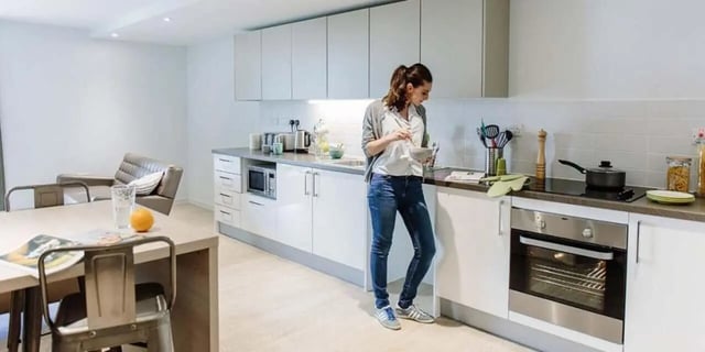 woman cooking at counter with dining table kitchen at CitySide in Leeds Student Accommodation