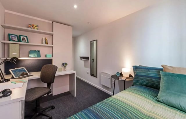 Desk with laptop chair shelves bed with pillows Bedroom at City Village in Coventry Student Accommodation