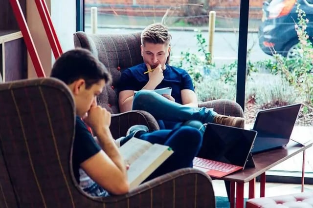 Students reading books and laptops in armchairs lounge at City Village in Coventry Student Accommodation