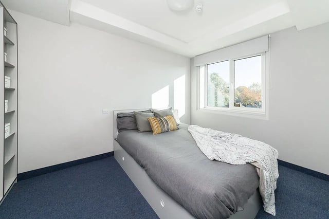 Bed with grey duvet and pillows bookshelf bedroom at Quayside Court in Newcastle Upon Tyne Student Accommodation