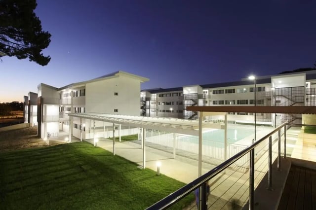 Modern white buildings with pool and grass exterior at Murdoch University Village in Perth Student Accommodation