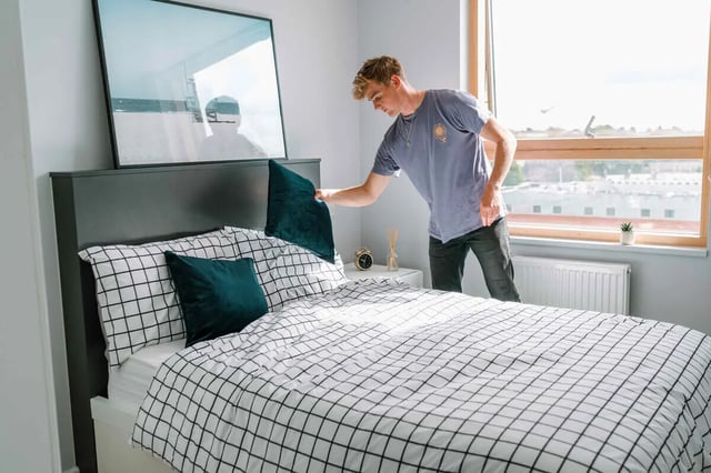 Man tidying bed with framed art bedroom at The Depot in Bath Student Accommodation