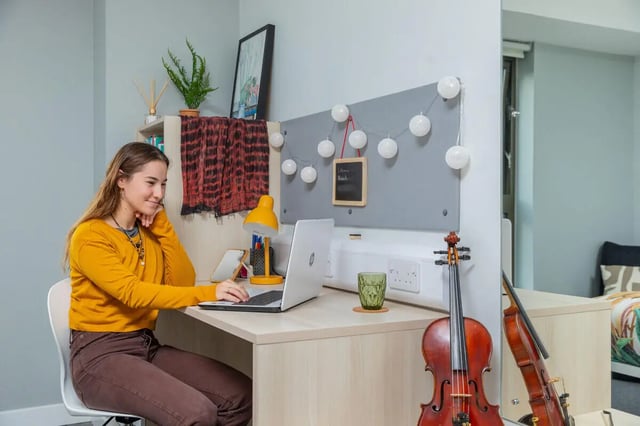 Student working on laptop violin by desk study area at Base in Glasgow Student Accommodation