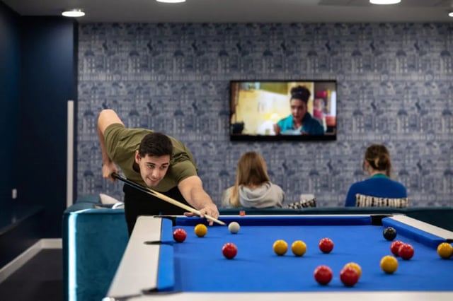 Man playing billiards with friends watching TV leisure area at Base in Glasgow Student Accommodation