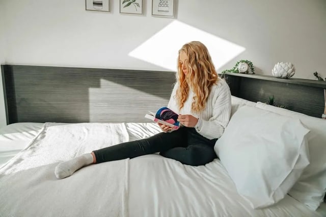 Woman reading book on bed white bedding bedroom at Avon Studios in Bath Student Accommodation