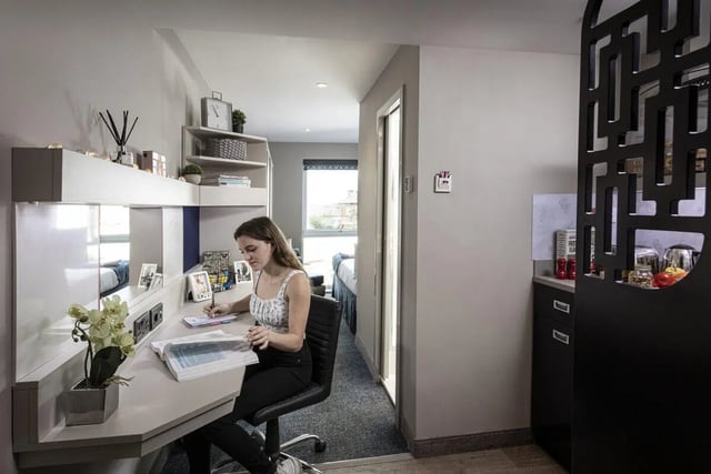 Student writing at desk with shelves and kitchen area bedroom at Study Inn Walnut Gardens Exeter in Exeter Student Accommodation