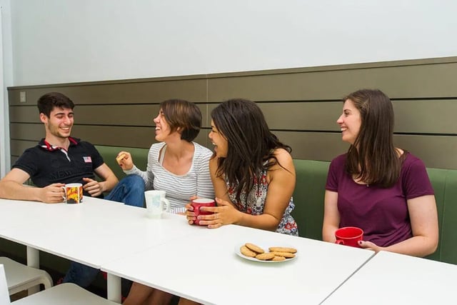 Four students laughing at a table with drinks and cookies common room at Graystacks in Nottingham Student Accommodation