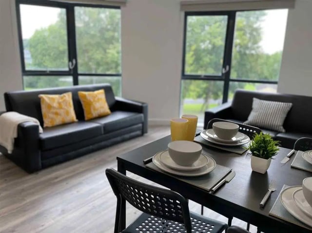 Black sofas dining table with place settings living room at Austin Hall in Leeds Student Accommodation