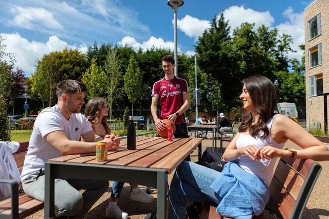 Students sitting at outdoor table with drinks and ball outdoor area at The Westwood in Galway Student Accommodation