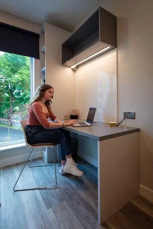 Woman using laptop at desk with overhead shelf Study area Image at The Westwood in Galway Student Accommodation