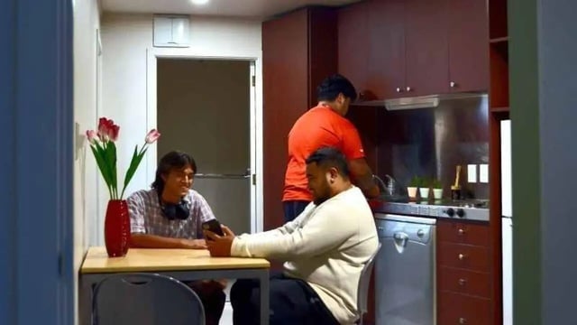 Three men in a kitchen with a table and flowers kitchen. at UniLodge Stafford House in Wellington Student Accommodation
